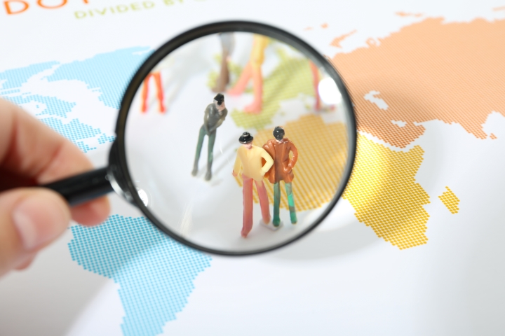 human figurines under the magnifying glass, sitting on colored paper world map