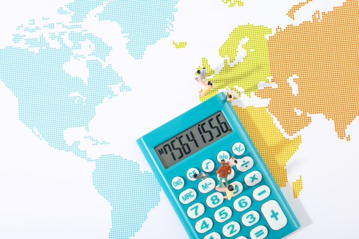 human figurines sitting on a calculator placed on the colored paper world map